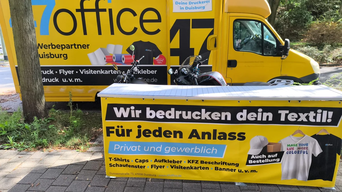 Gelbes 47office-Werbefahrzeug hinter einer bedruckten Werbetheke